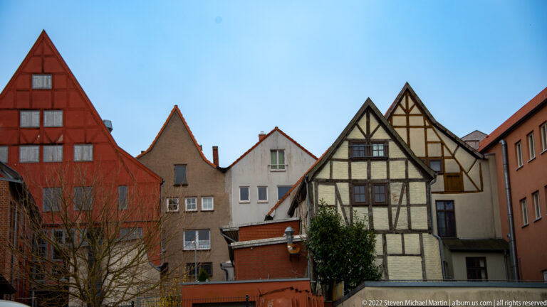 Half-timbered house among plastered gabled buildings and a red-painted house in Wismar’s historic center.