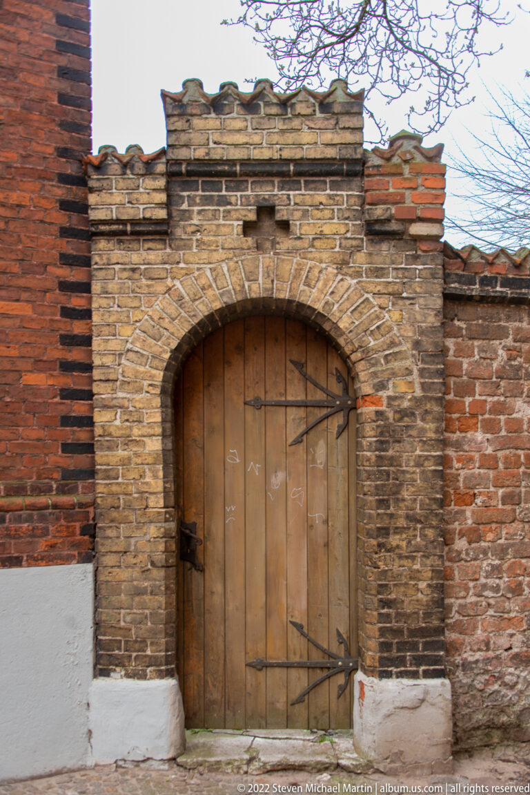 Round-arched wooden door with iron strap hinges set in weathered brick and stone masonry.