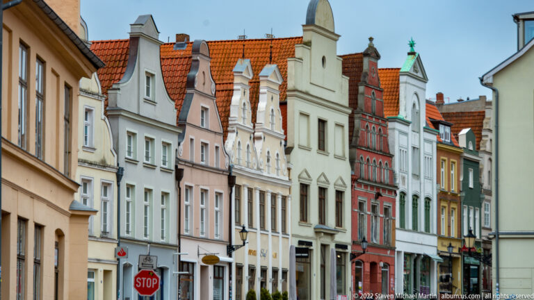 Colorful row of narrow historic houses with varied decorative gables and red-tiled roofs along a Wismar street.