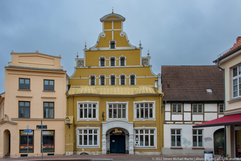 Mustard-yellow historic townhouse with ornate stepped-curved gable, white-trimmed windows, and a dark central doorway.