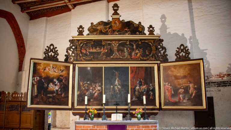 Large multi-panel painted altarpiece with gilded frames and ornate cresting above a brick altar.