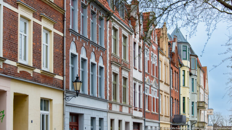 Row of narrow historic townhouses in brick and stucco with varied windows, bays, and rooflines.