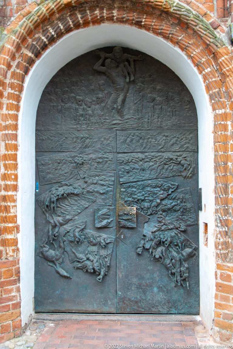 Large bronze relief doors beneath a brick arch, covered with figures and narrative scenes.