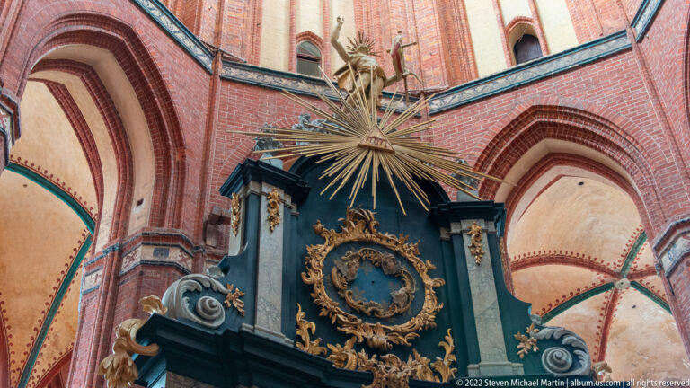 Gilded starburst and scrolling ornament crown a dark altar beneath high red-brick vaults.