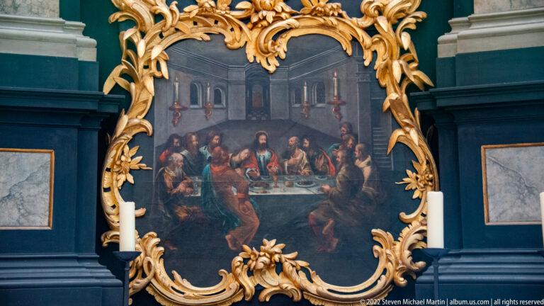 Last Supper painting with Christ and apostles around a table, surrounded by an elaborate gilded scrolling frame.