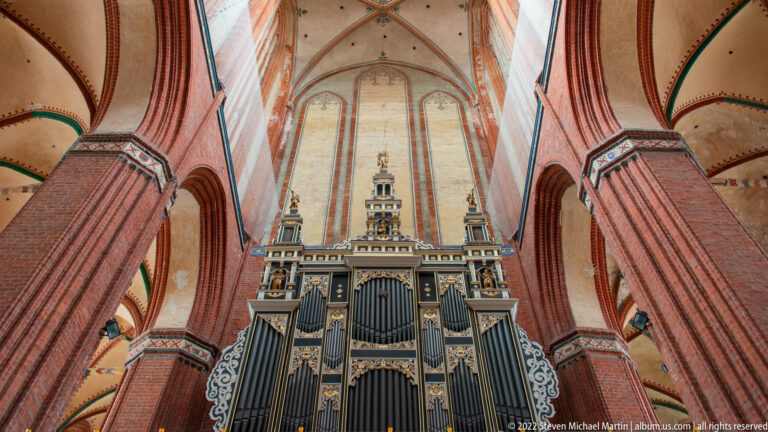 Large ornate pipe organ with tall ranks of pipes and gilded details framed by massive red-brick church piers.