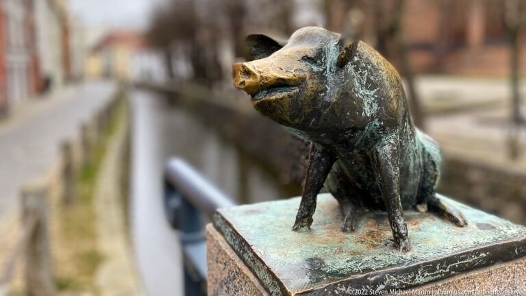 Upright bronze pig with lifted snout sits on a bridge post above Wismar's canal.