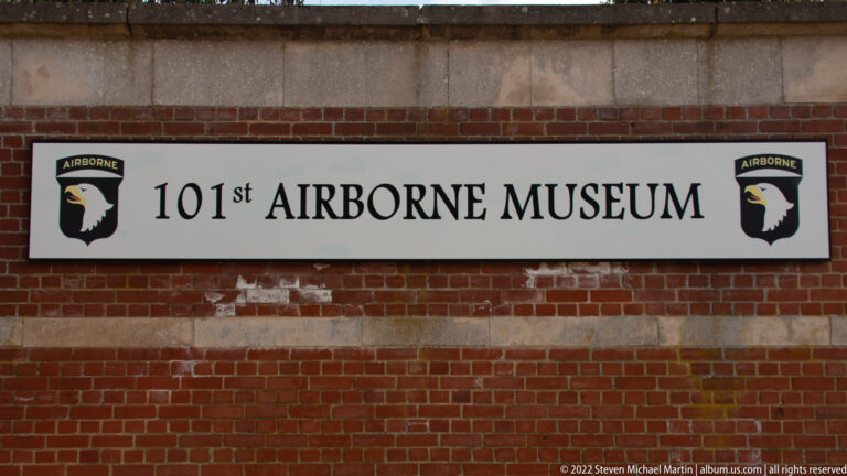 White 101st Airborne Museum sign with eagle emblems mounted on a red-brick wall.