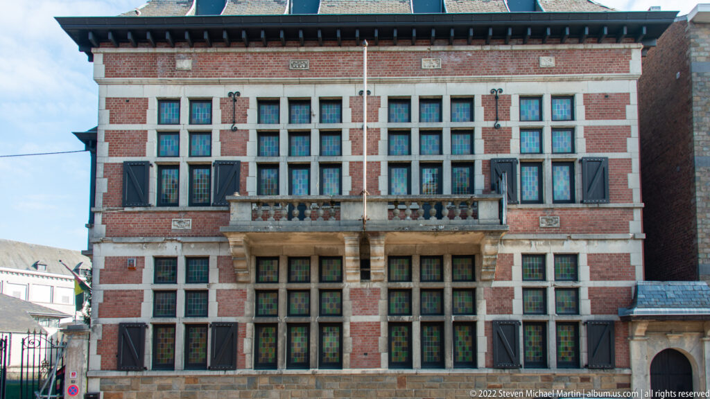 Symmetrical red-brick museum façade with stone trim, rows of windows, shutters, balcony, and central entrance.