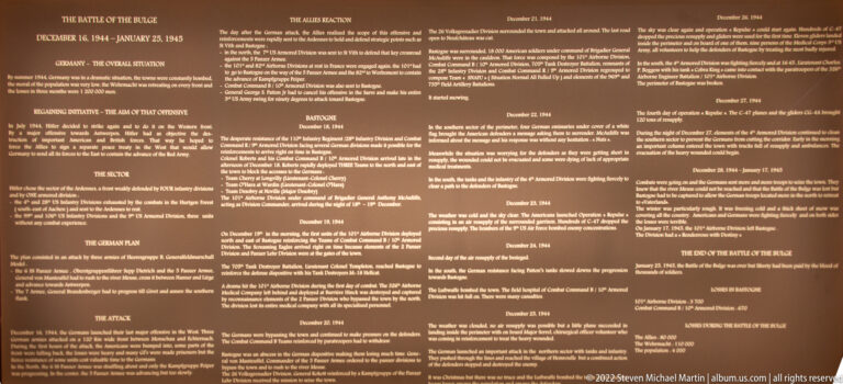 Large brown museum panel filled with dated sections and text describing stages of the Battle of the Bulge.