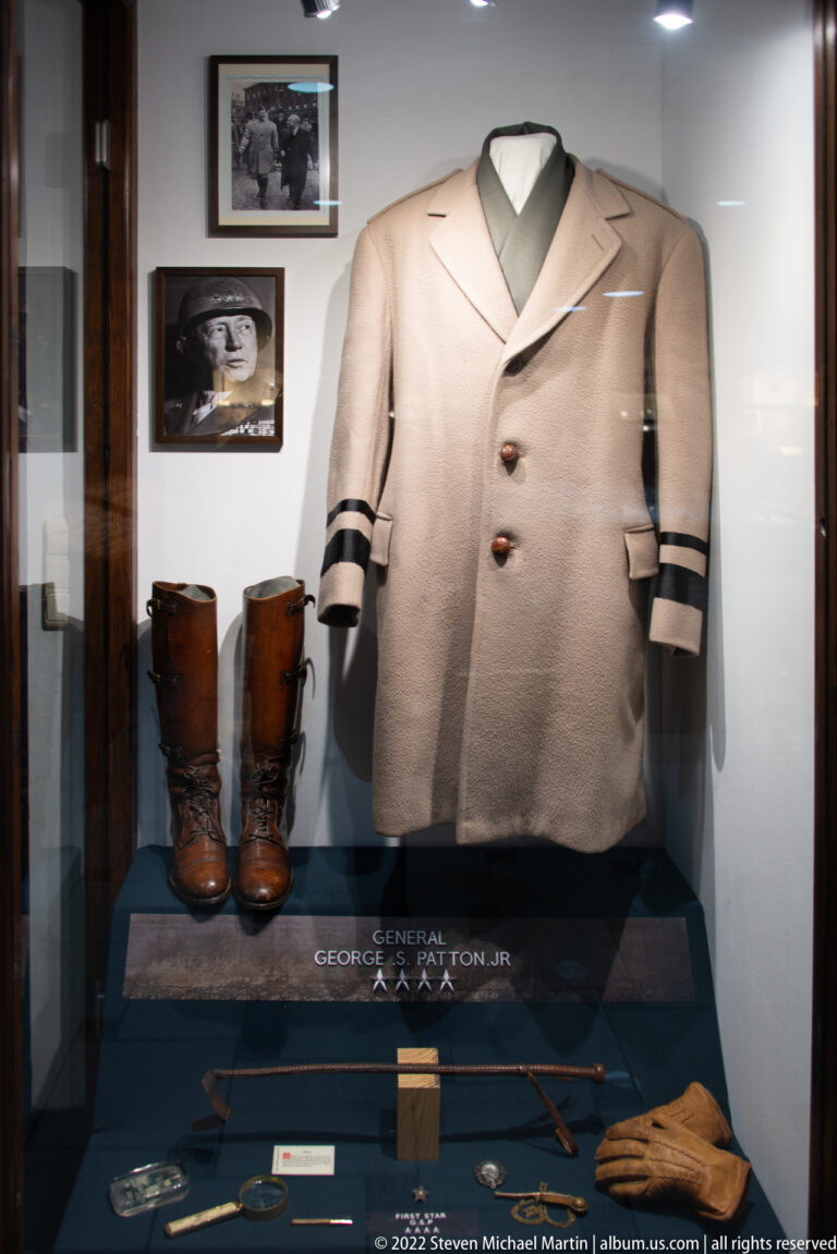 Pale double-breasted officer coat and tall boots displayed above a label naming General George S. Patton Jr.