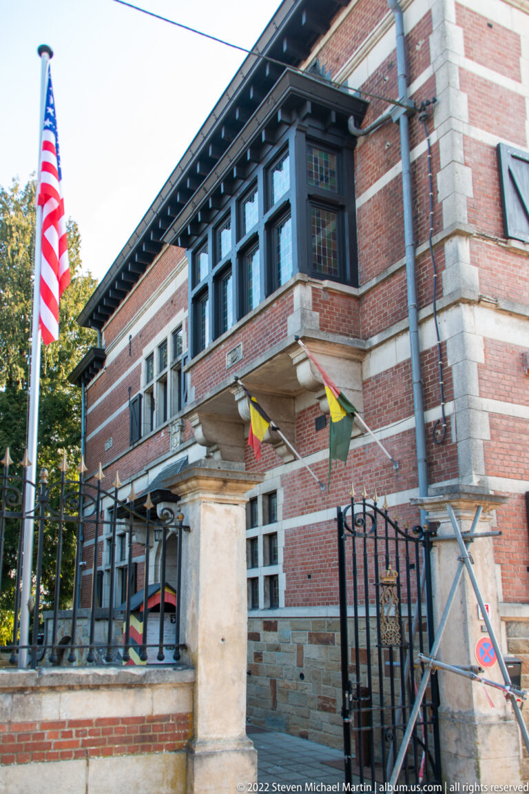 Red-brick museum façade with stone trim, dark windows, American and Belgian flags, and scaffolding.