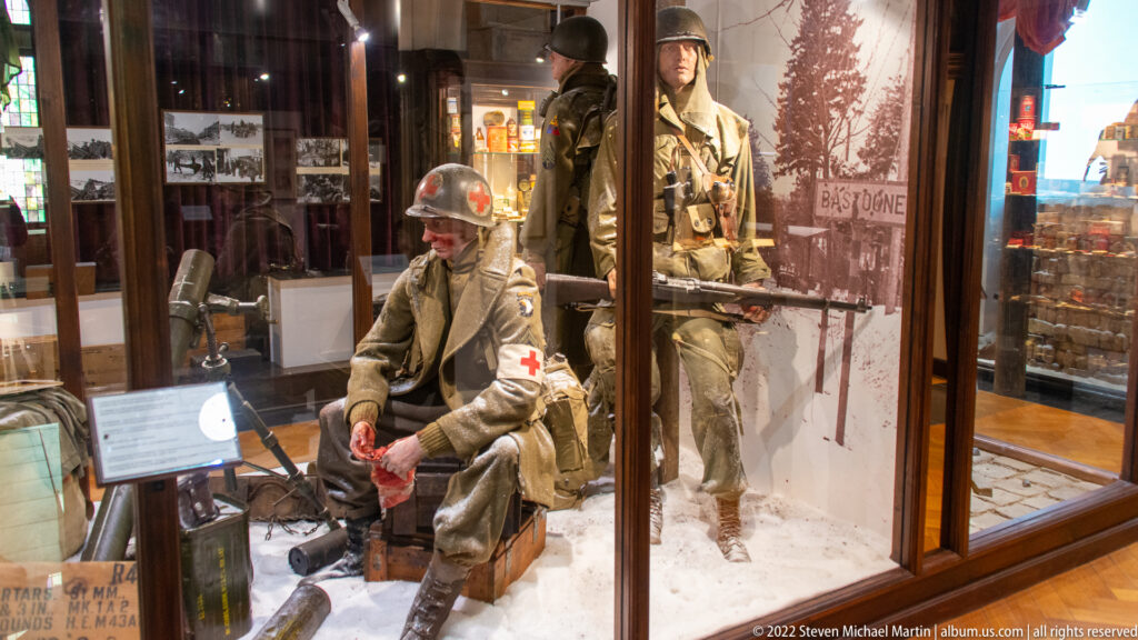 Winter museum diorama with a seated medic wearing a Red Cross armband and soldiers standing in snow behind him.