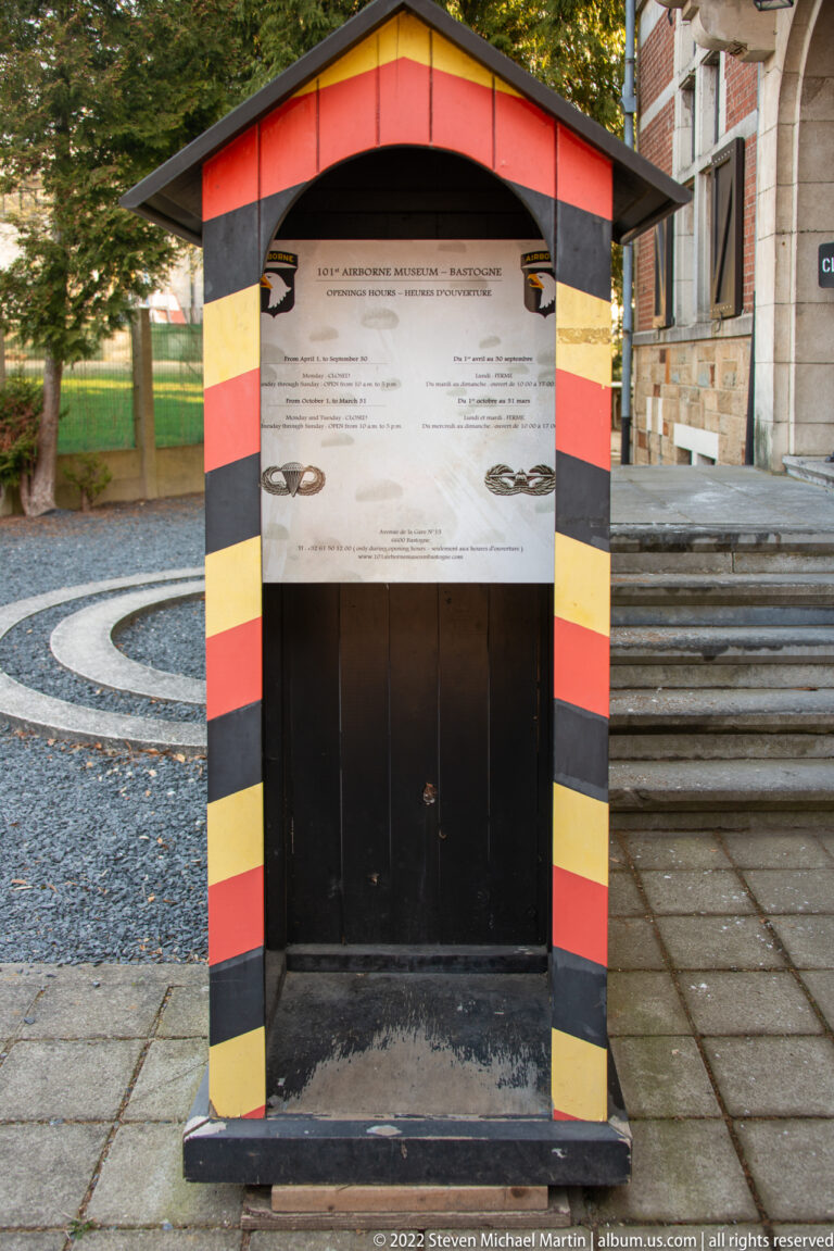 Outdoor information panel beneath a small shelter striped black, yellow, and red.