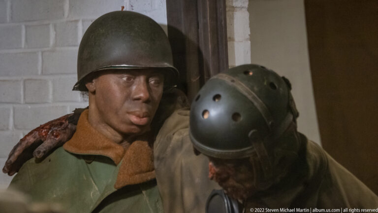 Close-up of two helmeted soldiers with simulated facial and shoulder wounds in a museum battle diorama.