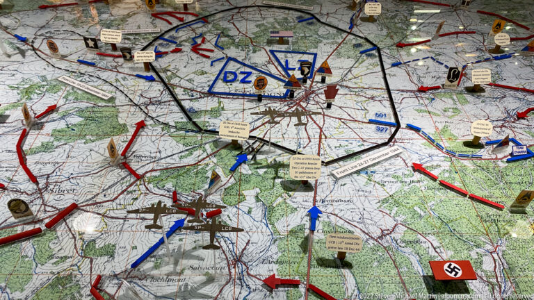 Operational map covered with red and blue arrows, unit markers, labels, and battle symbols around Bastogne.