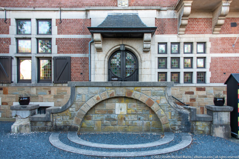 Arched doorway centered in a red-brick and stone façade above a semicircular forecourt feature.