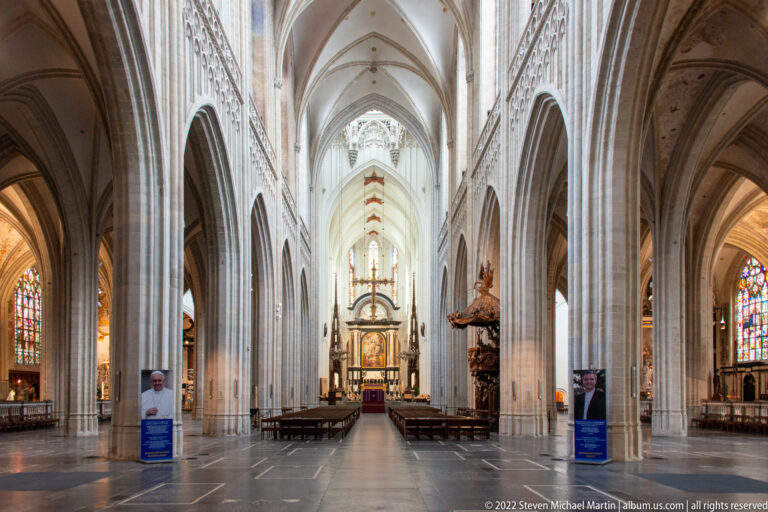 Long central nave of Antwerp Cathedral with clustered columns, pointed arcades, rib vaults, stained glass, and distant high altar.