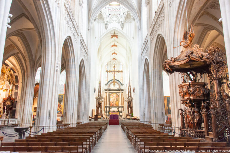 Central cathedral nave with distant altar and an elaborate dark carved wooden pulpit filling the right foreground.