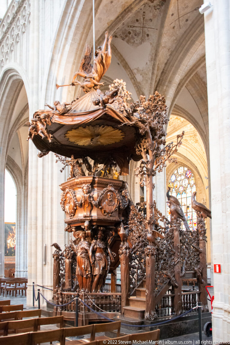 Elaborately carved dark wooden pulpit with figures, foliage, and raised platform inside Antwerp Cathedral.