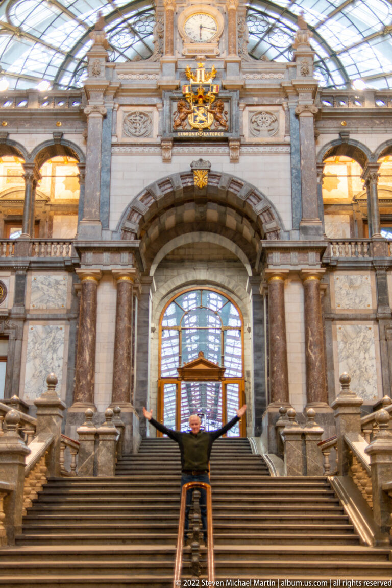 Person with arms outstretched on the broad stone staircase inside Antwerp-Central Station.
