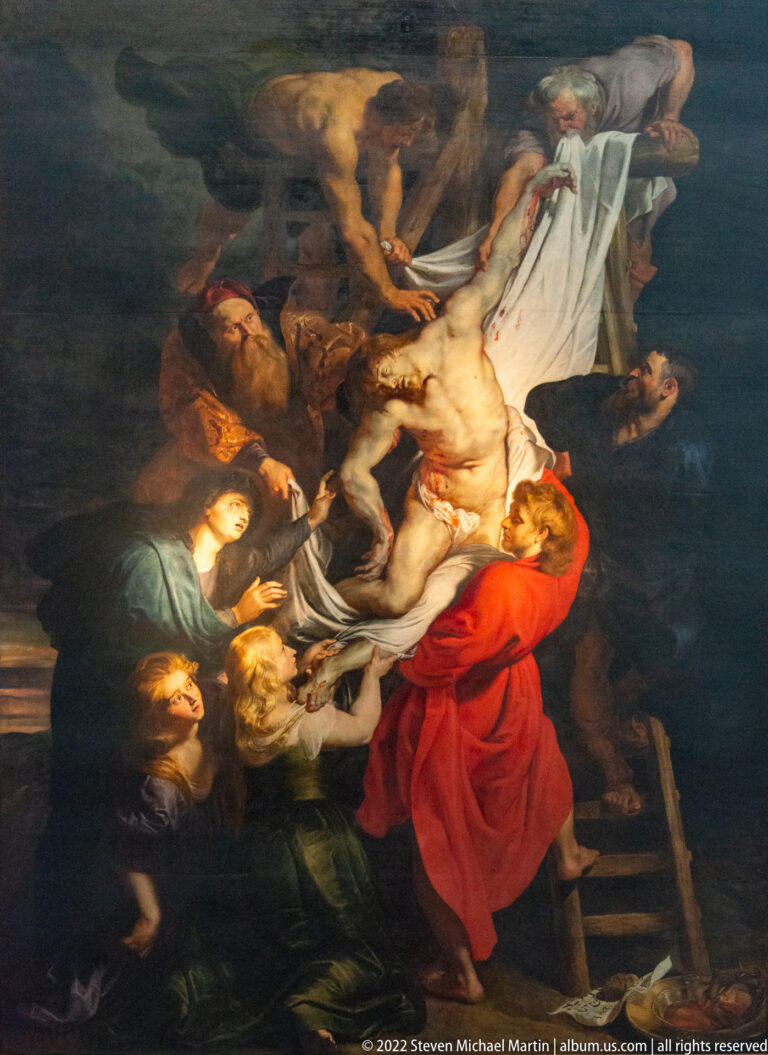Central panel of Rubens’s The Descent from the Cross with Christ’s pale body lowered among figures in red and dark clothing.