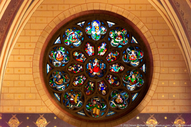 Round stained-glass rose window with a central enthroned figure and concentric rings of colorful figural medallions.