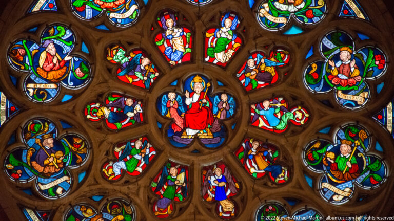 Close detail of a stained-glass rose window with an enthroned central figure surrounded by colorful narrative medallions.