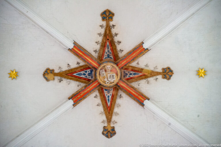 Red, blue, and gold star-shaped ceiling boss with central portrait medallion at the intersection of pale vault ribs.