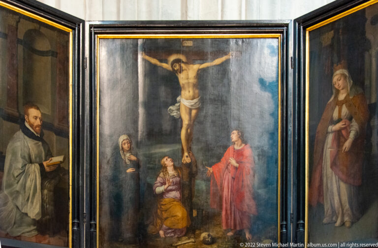 Open Crucifixion triptych with Christ on the cross in the center and standing donor or saint figures on the side wings.