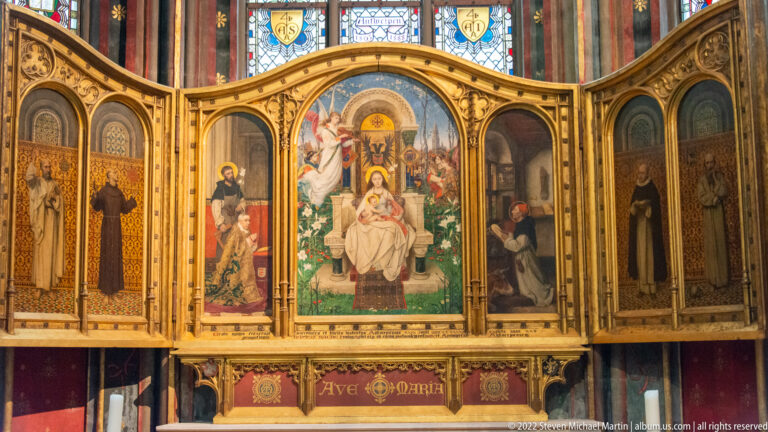 Close view of gilded Marian altarpiece with Virgin and Child at center, saints on side panels, and Ave Maria below.
