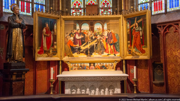 Open Passion triptych above a carved stone altar, with a crowded central scene and standing saints on both wings.