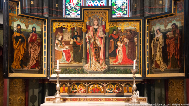 Multi-panel altarpiece with Virgin and Child at center, painted saints and narrative scenes, gilded tracery, and altar candles.