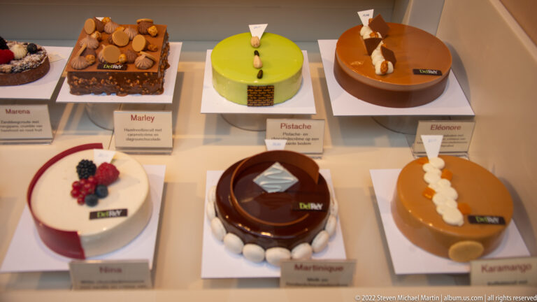 Six modern round cakes in green, caramel, chocolate, and cream finishes displayed with printed flavor cards.
