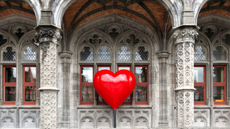 Large glossy red heart mounted on an ornate gray stone facade with carved columns and arched windows.