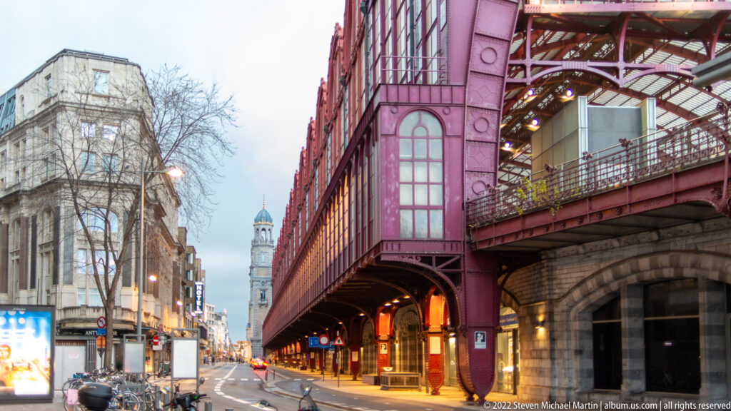 Red elevated railway structure and masonry arches running beside an Antwerp street at dusk.