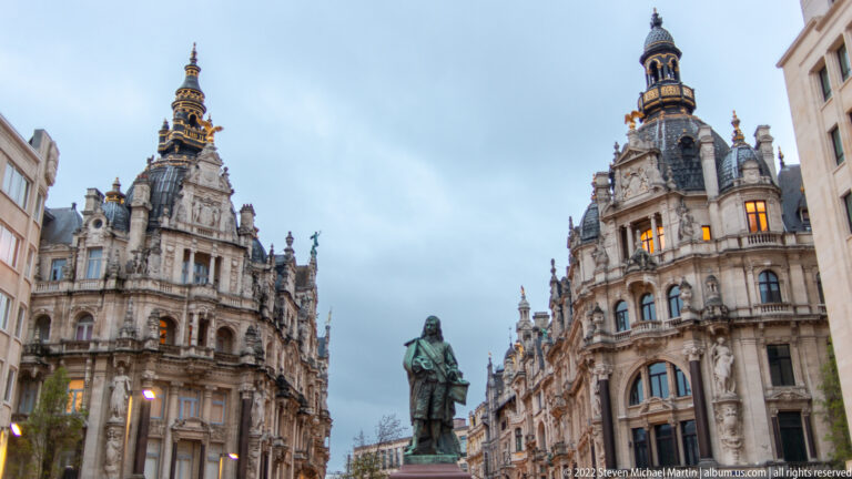 Bronze statue of David Teniers the Younger framed by ornate historic buildings at Teniersplaats in Antwerp.