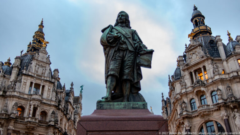 Close view of the bronze David Teniers the Younger statue against ornate buildings at Teniersplaats.