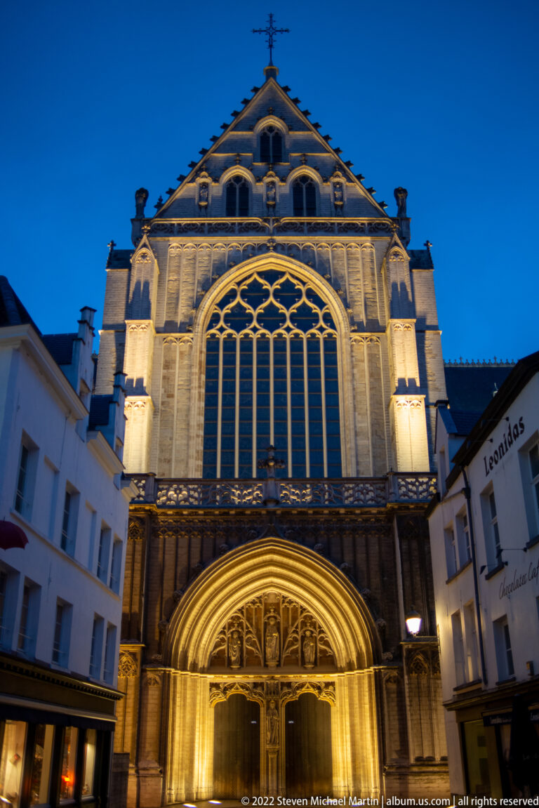 Illuminated Gothic church façade with a large traceried window and pointed-arch portal at blue hour.