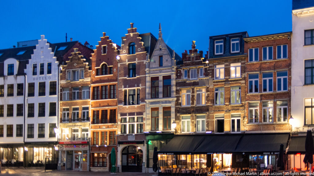 Illuminated narrow historic façades with stepped and ornate gables lining Antwerp’s Grote Markt at dusk.