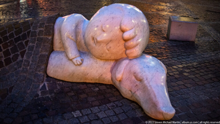 White stone sculpture of Nello and Patrasche sleeping together on cobblestones in central Antwerp.
