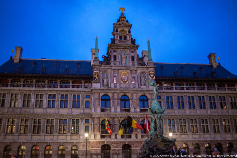 Antwerp City Hall illuminated at night behind the Brabo Fountain and flags on the Grote Markt.