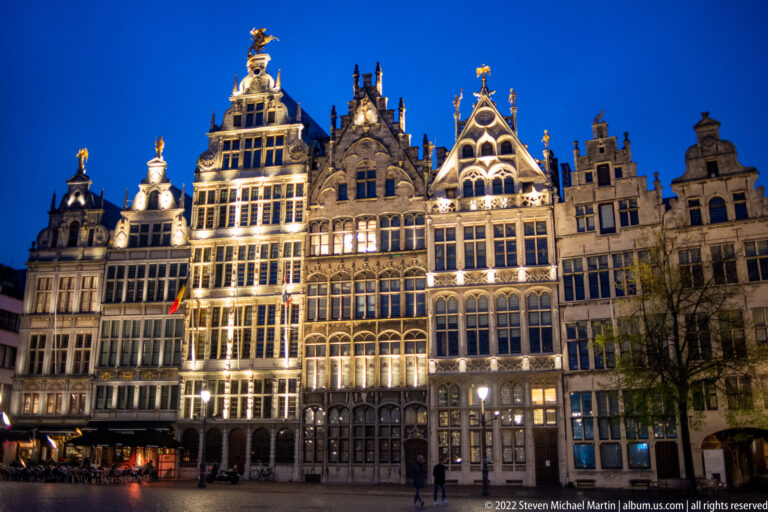 Illuminated guildhouses with ornate gables and gilded rooftop figures on Antwerp’s Grote Markt.