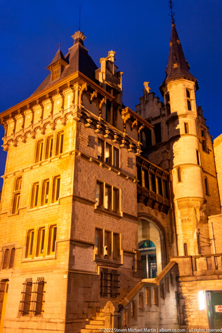 Floodlit historic building with a corner turret, rows of windows, and broad exterior steps at night in Antwerp.