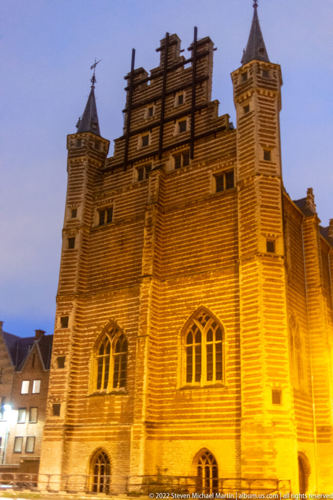 Vleeshuis in Antwerp with striped brick-and-stone masonry, stepped gable, turrets, and pointed windows at dusk.