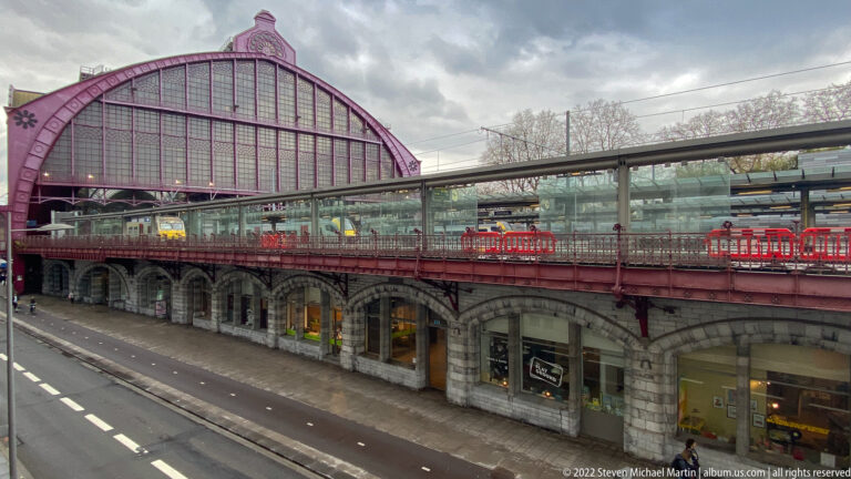 Antwerp-Central train shed above elevated tracks and street-level arches, with a modern glazed walkway beside it.