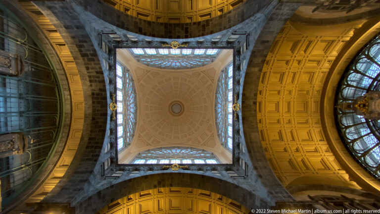 Upward view inside Antwerpen-Centraal where monumental arches frame a pale central vault and coffered ceilings.