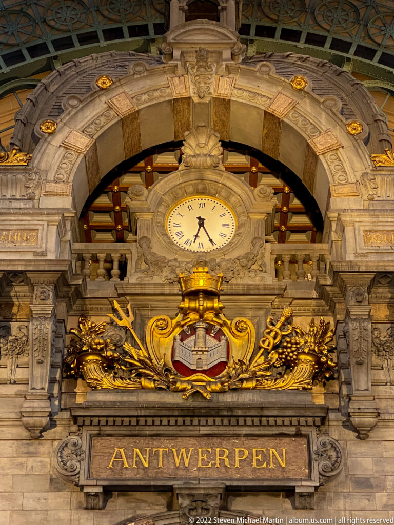Close view of Antwerpen-Centraal clock above gilded Antwerp crest and ANTWERPEN inscription in ornate stonework.