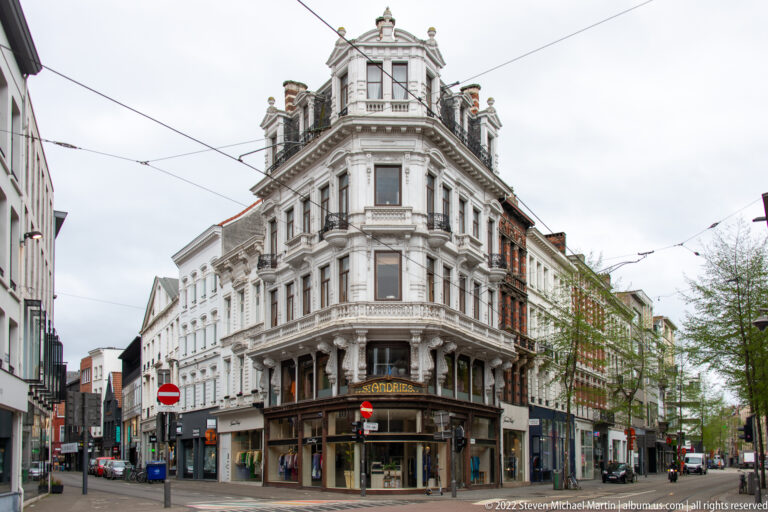 Ornate white historic corner building with rounded bay, balconies, sculpted roofline, shops, and tram wires overhead.