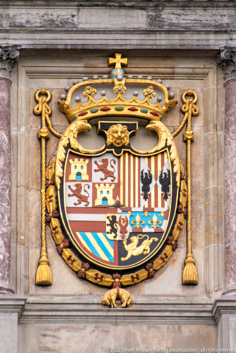Large quartered heraldic shield with crown, gold scrollwork, lions, castles, stripes, and multiple colored fields.